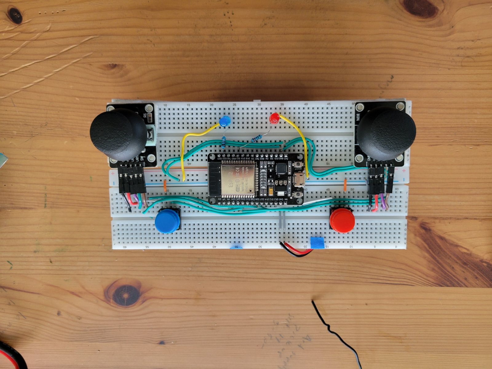 Head-on view of the custom transmitter: an ESP32 development board wired on a breadboard between two analogue thumbstick gimbals sitting along the lower edge, with red and blue pushbuttons.