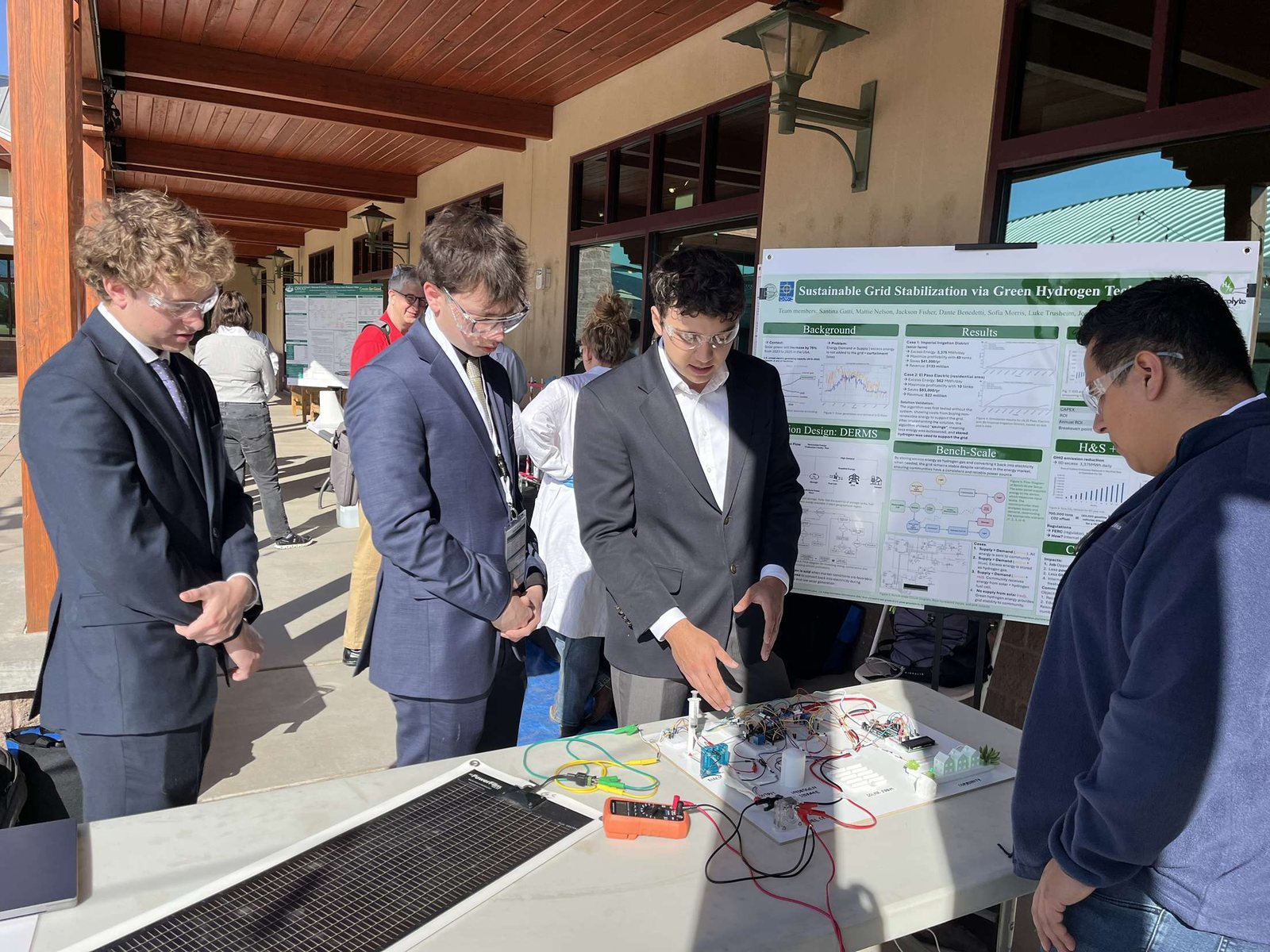 The team presenting the bench-scale system at the WERC Environmental Design Contest, with the demonstration board and solar panel on the table and the project poster behind them.